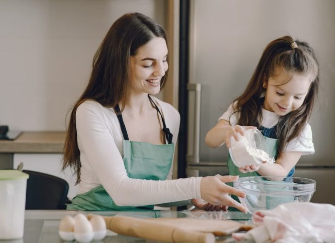 A joyful mother and daughter bonding while baking in the kitchen, smiling and enjoying the activity.